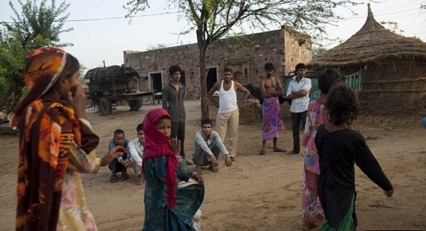 Girls pass through an Indian village watched by men.  