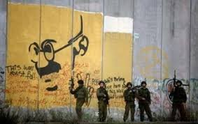 Israeli soldiers stand near the  Apartheid wall with Gandhi's portrait on the so-called separation barrier. 