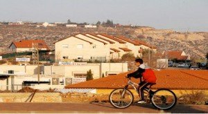 A boy rides his bicycle past houses in the Israeli settlements of Ofra, in the occupied West Bank. -- File photo