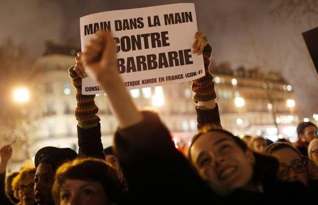 A woman holds a placard that reads, "Hand in hand against barbarity", during a vigil to pay tribute to the victims of a shooting by gunmen at the offices of weekly satirical magazine Charlie Hebdo in Paris, at Republique square January 7, 2015. REUTERS/Youssef Boudlal