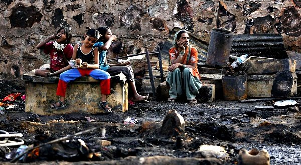 A family sits amid the burnt debris of their hut after a fire broke out in a slum area in New Delhi. Rreuters file/Adnan Abidi 