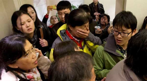 A woman, center, surrounded by media covers her mouth on her arrival at a hotel which is prepared for relatives or friends of passengers aboard a missing airplane, in Beijing, China on March 8, 2014. AP