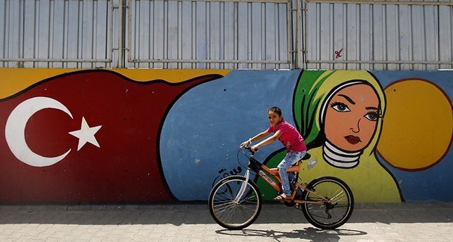 A child cycles past graffiti at the Öncüpınar camp for Syrian refugees next to the border crossing with Syria, near the town of Kilis in southeastern Turkey, Monday, June 20, 2016 (AP Photo)